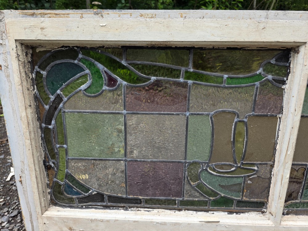 A wide rectangular antique leaded glass transom window featuring three sections of green, amber, blue, and red coloured glass with Art Nouveau scrollwork motifs set in a timber frame. View V