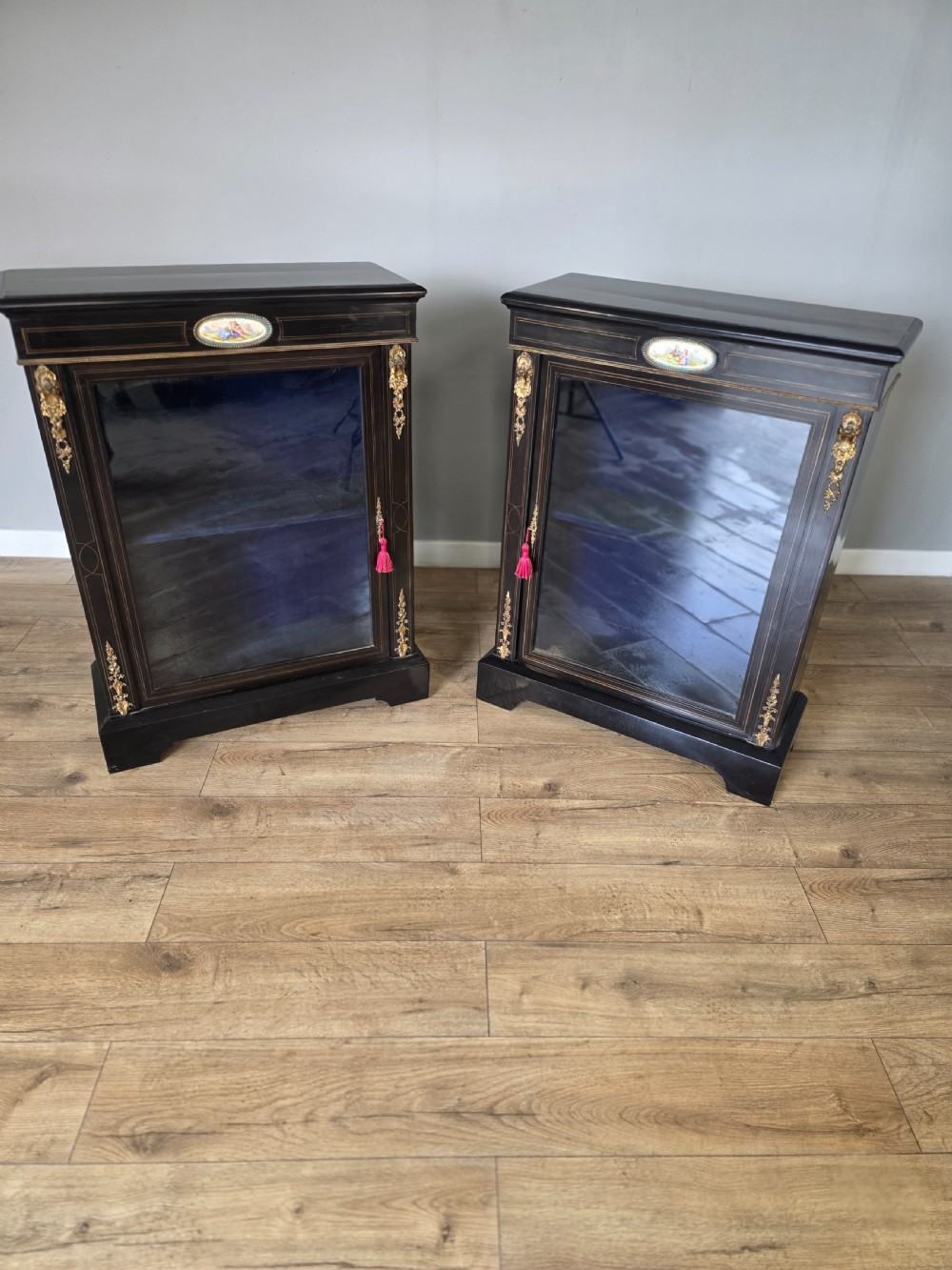 A pair of Victorian ebonised wooden pier cabinets featuring single glazed doors, gilt metal ormolu corner mounts, and oval porcelain plaques. View III