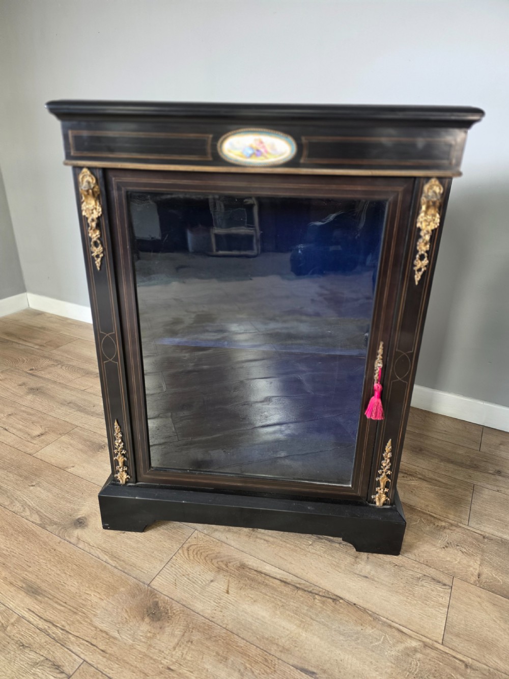 A pair of Victorian ebonised wooden pier cabinets featuring single glazed doors, gilt metal ormolu corner mounts, and oval porcelain plaques. View IV