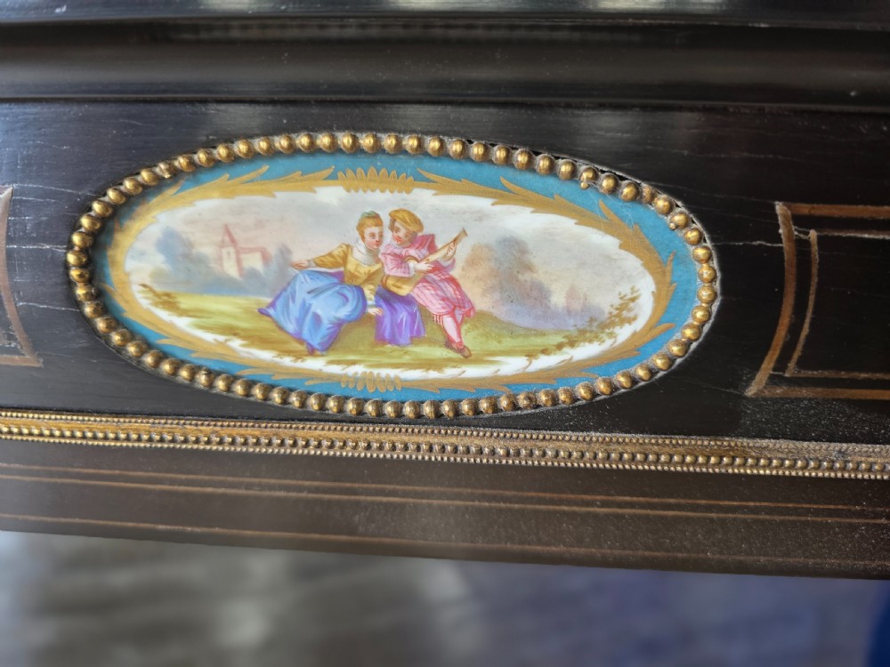 A pair of Victorian ebonised wooden pier cabinets featuring single glazed doors, gilt metal ormolu corner mounts, and oval porcelain plaques. View VII