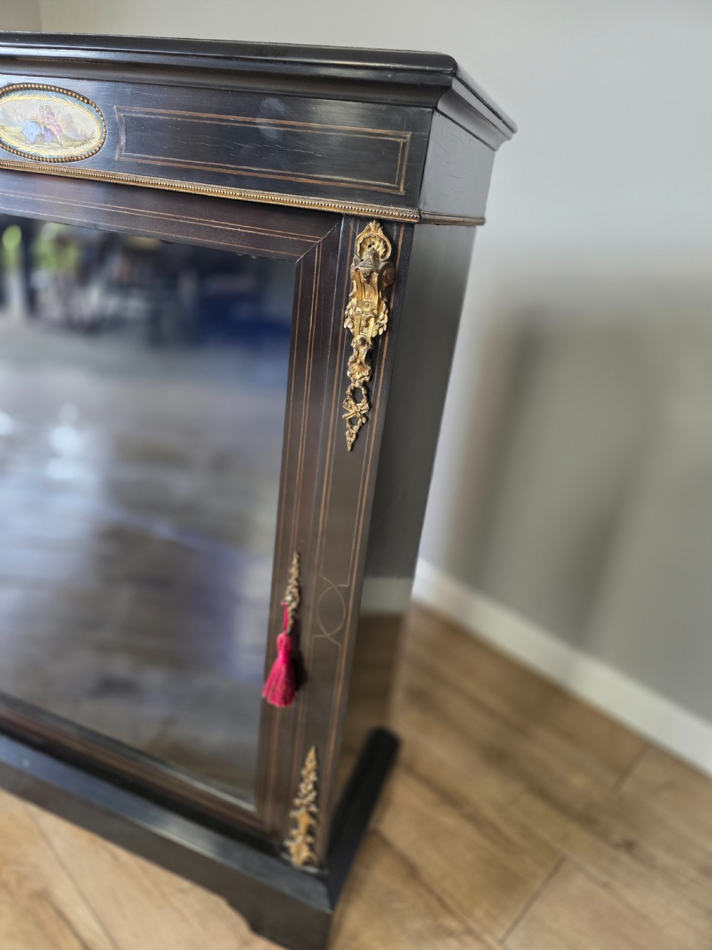 A pair of Victorian ebonised wooden pier cabinets featuring single glazed doors, gilt metal ormolu corner mounts, and oval porcelain plaques. View VIII