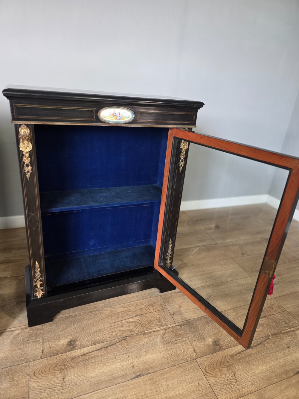 A pair of Victorian ebonised wooden pier cabinets featuring single glazed doors, gilt metal ormolu corner mounts, and oval porcelain plaques. View XIII