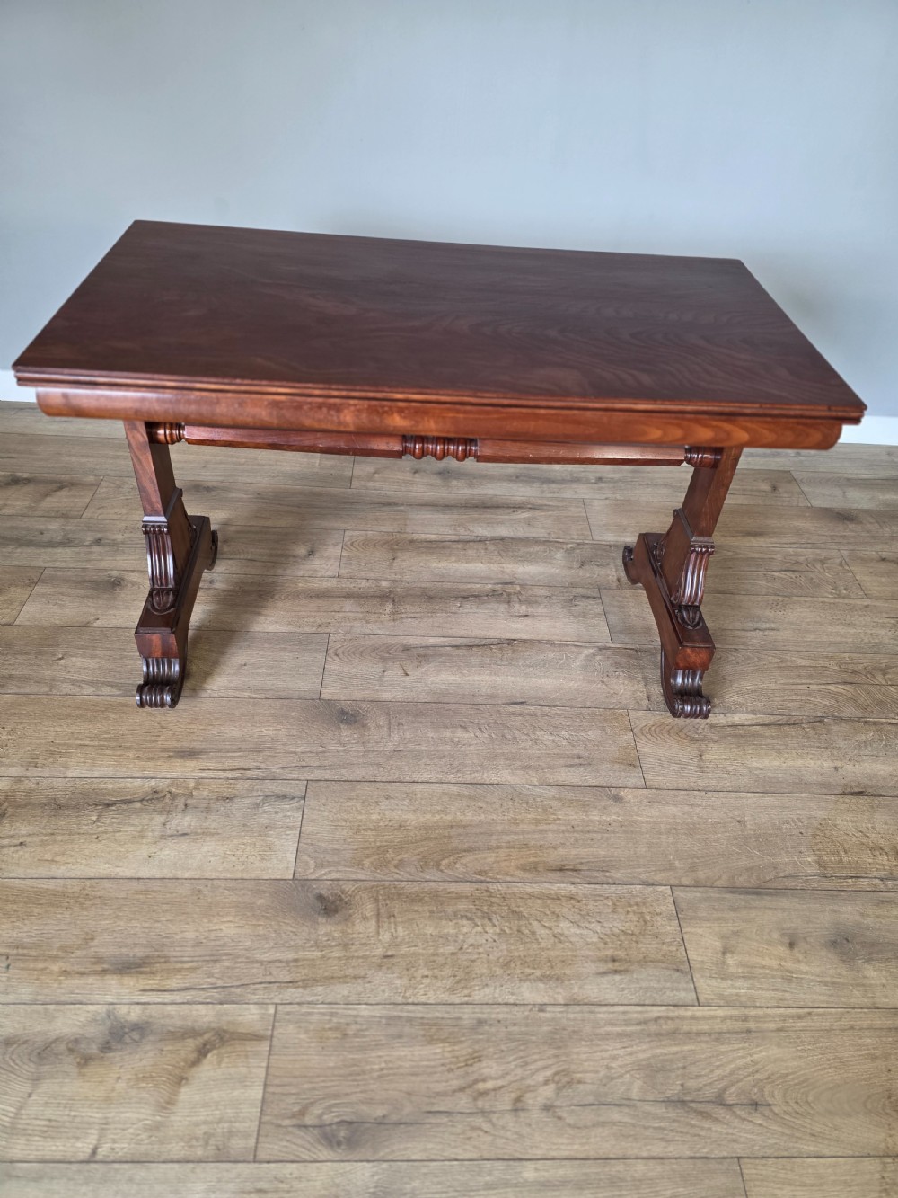 An early Victorian mahogany side table featuring a rectangular top, a central turned stretcher, and carved trestle feet resting on a light wood floor. View III