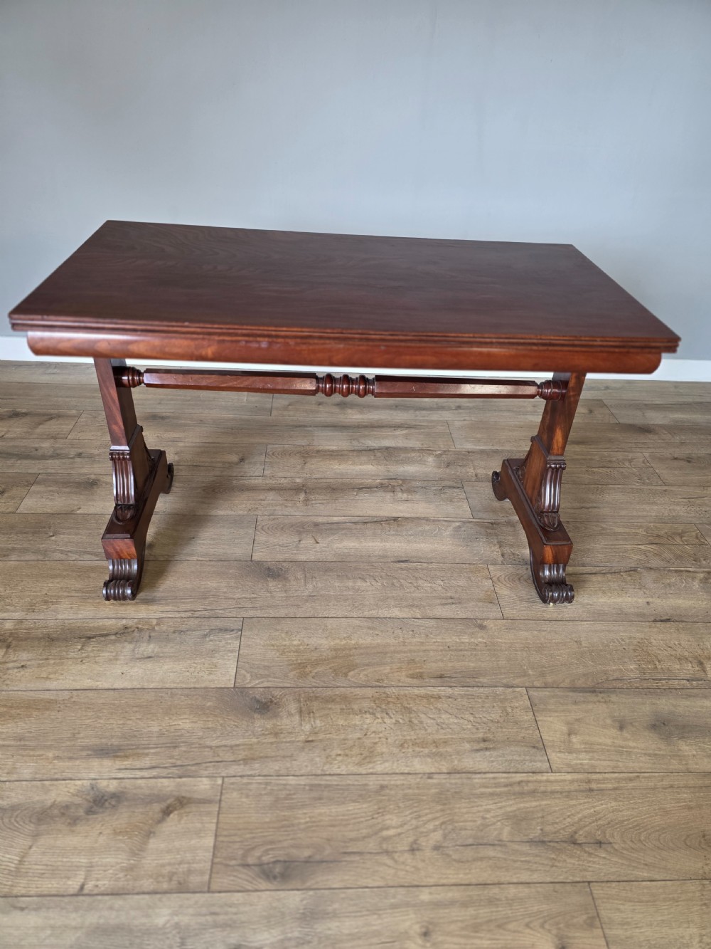An early Victorian mahogany side table featuring a rectangular top, a central turned stretcher, and carved trestle feet resting on a light wood floor. View XI