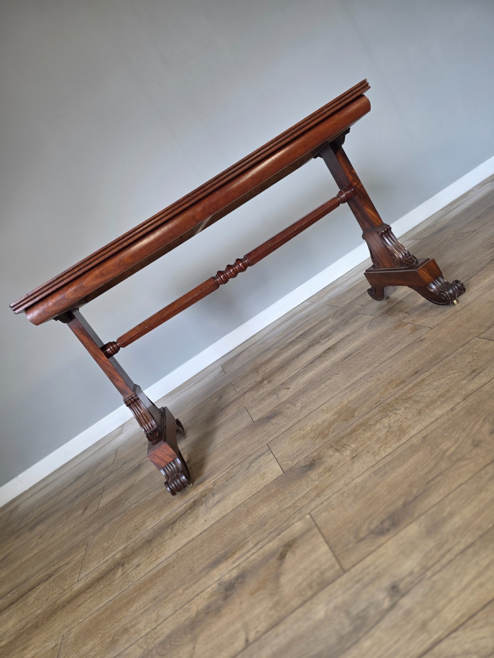 An early Victorian mahogany side table featuring a rectangular top, a central turned stretcher, and carved trestle feet resting on a light wood floor. View XIII