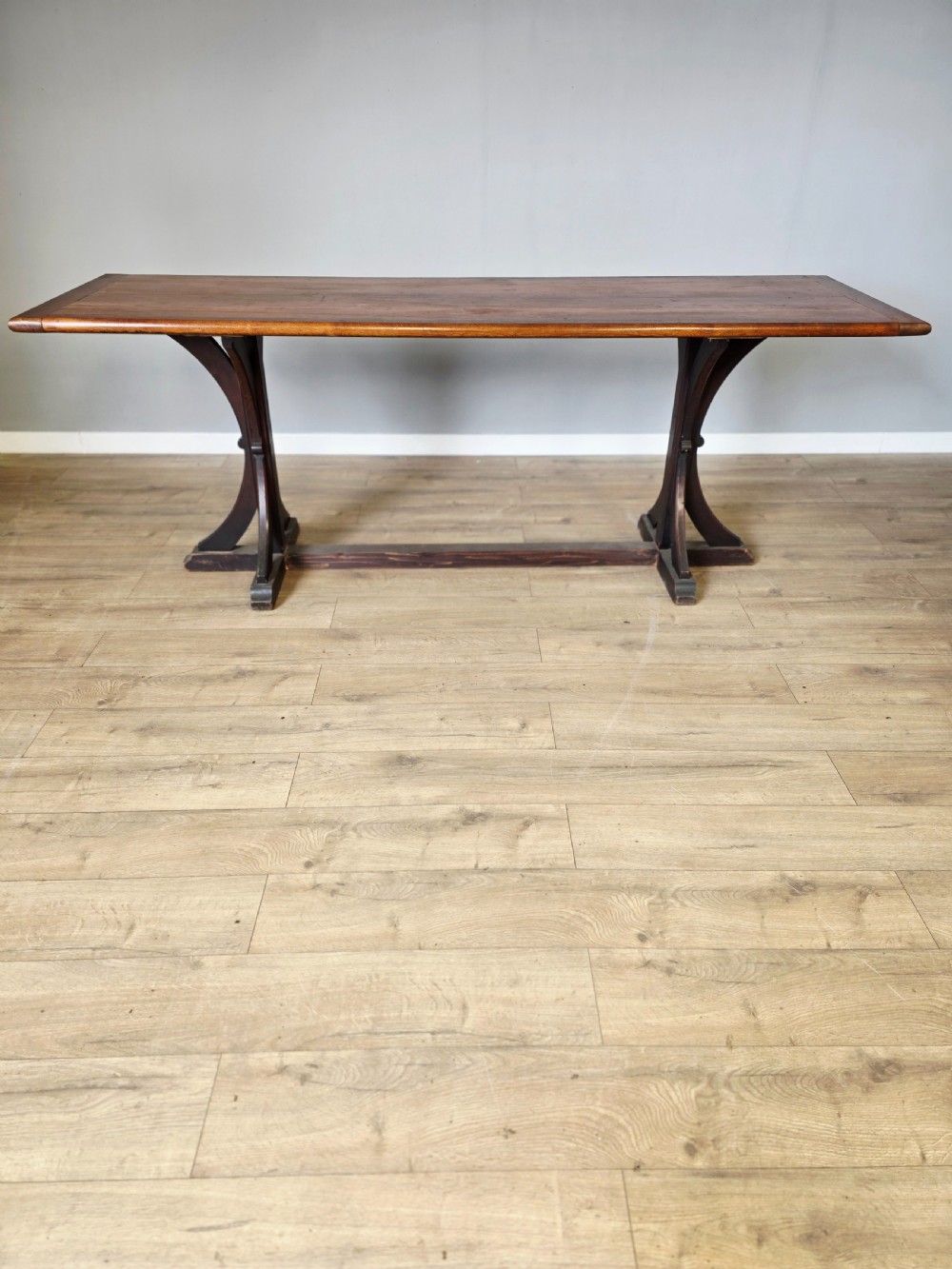 A long Victorian pitch pine centre serving table featuring a smooth rectangular top supported by curved trestle legs and a central stretcher base.