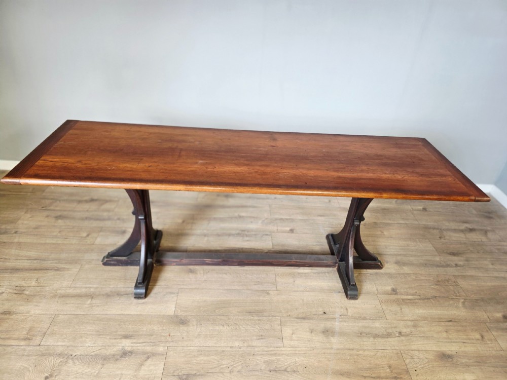 A long Victorian pitch pine centre serving table featuring a smooth rectangular top supported by curved trestle legs and a central stretcher base. View II