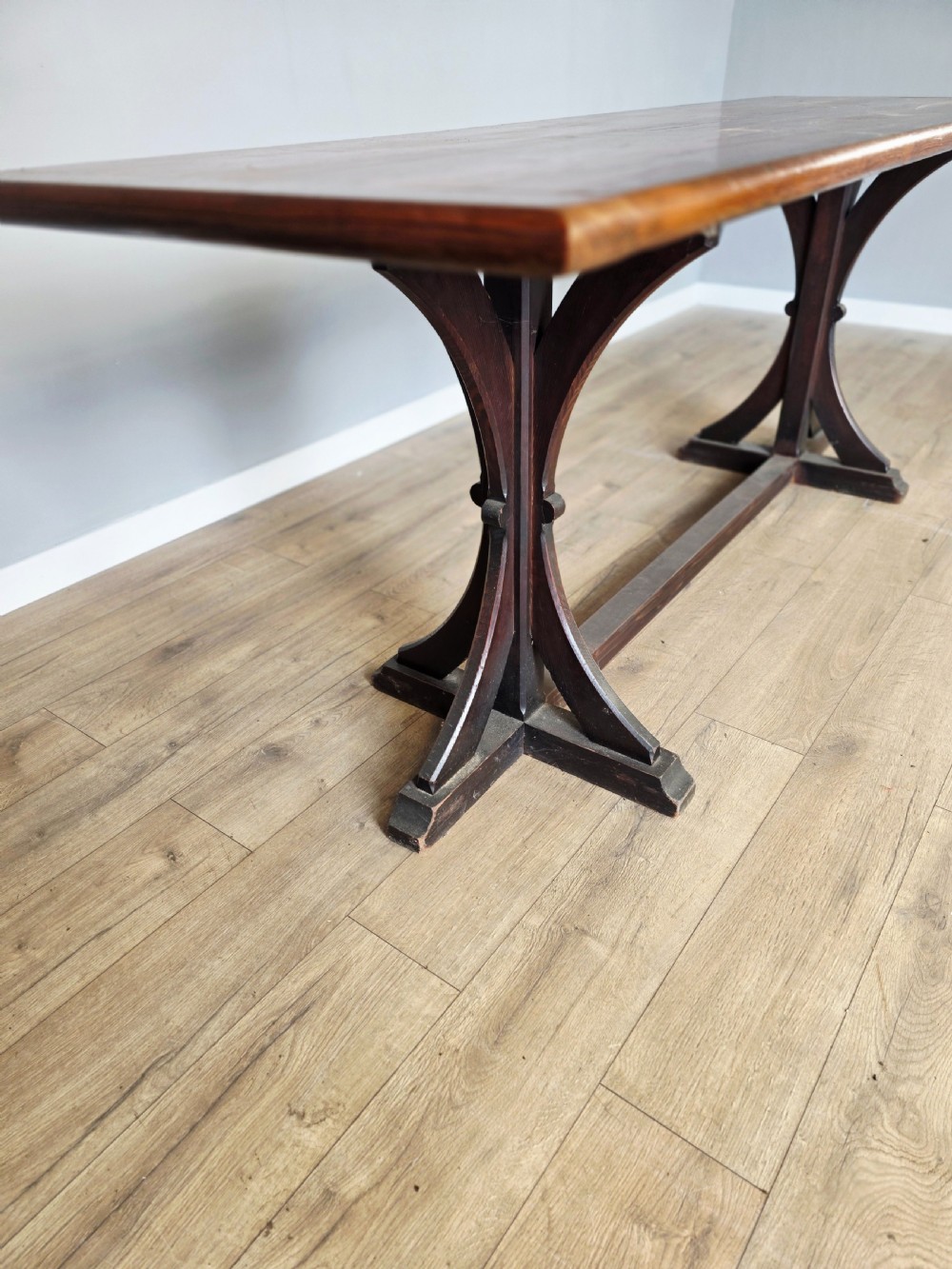 A long Victorian pitch pine centre serving table featuring a smooth rectangular top supported by curved trestle legs and a central stretcher base. View V