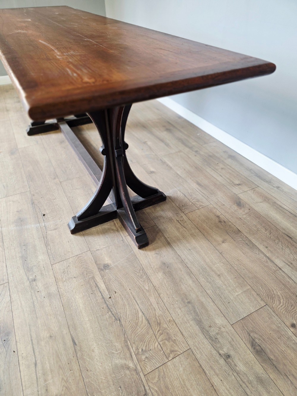 A long Victorian pitch pine centre serving table featuring a smooth rectangular top supported by curved trestle legs and a central stretcher base. View VI