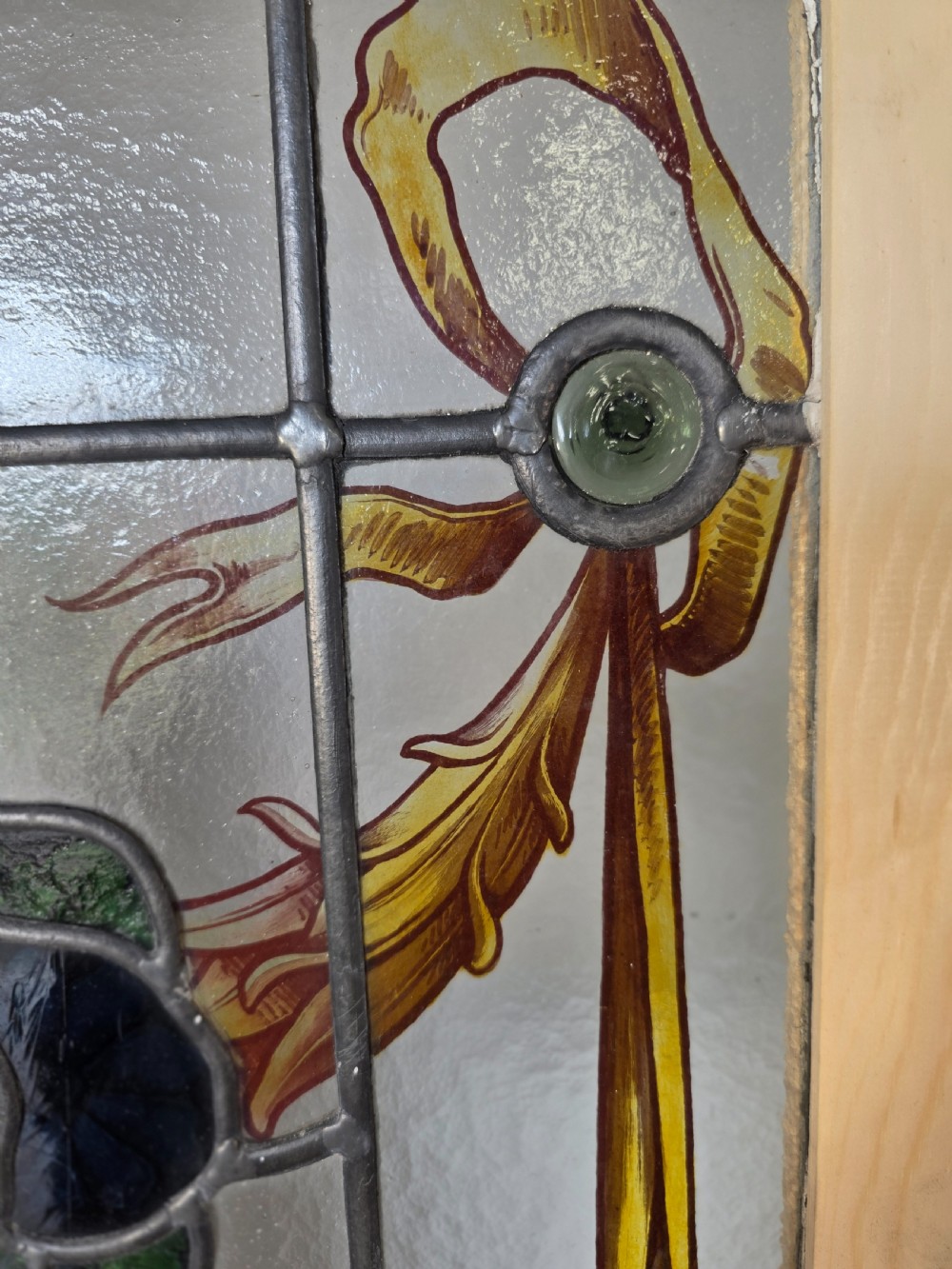 An antique rectangular leaded glass window panel featuring hand-painted red flowers, green leaves, yellow ribbon swags, and small glass bullseyes set within a wooden frame. View IV