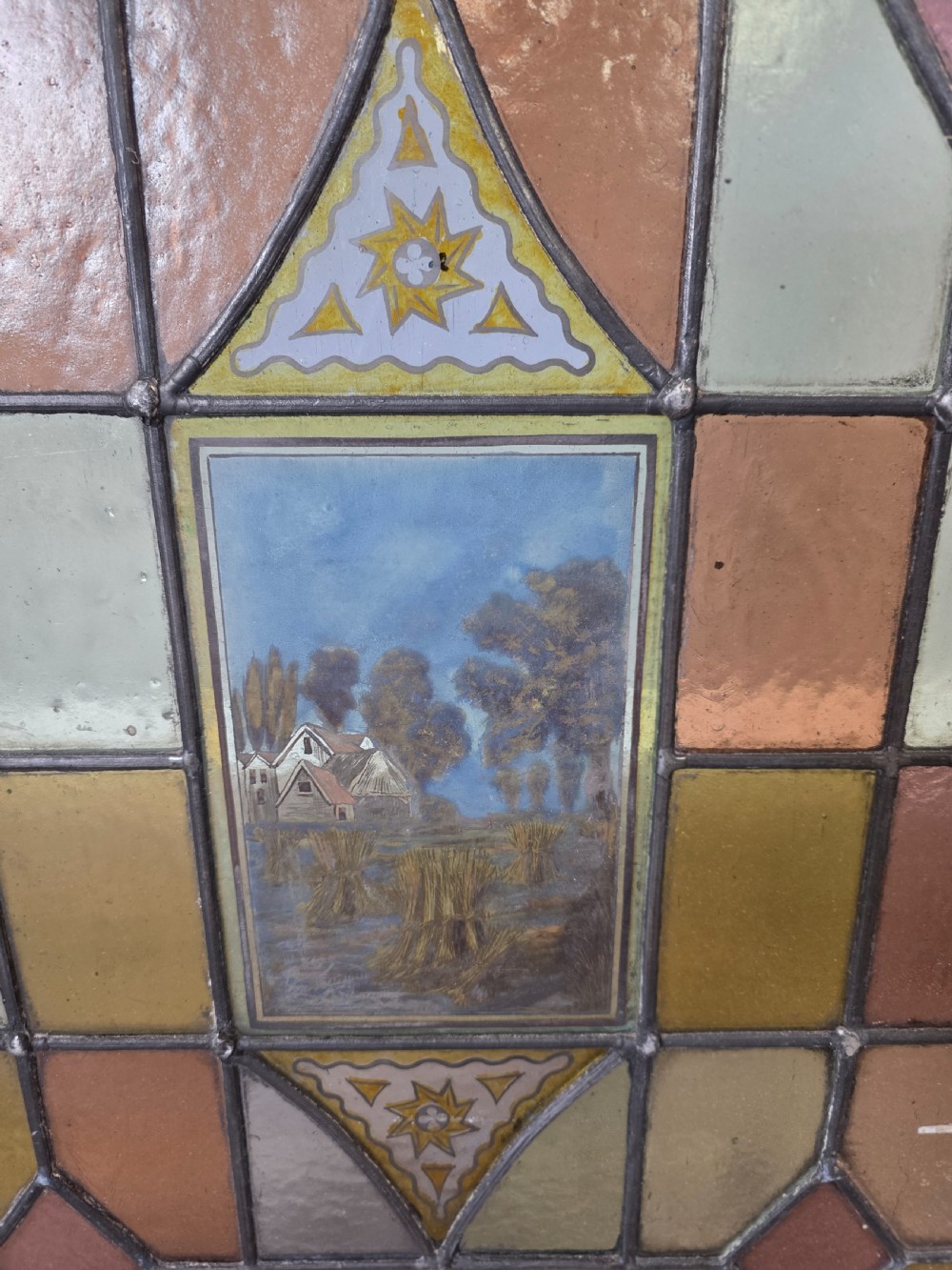 A rectangular leaded stained glass panel featuring geometric multicoloured glass sections and a central hand-painted country landscape. View II