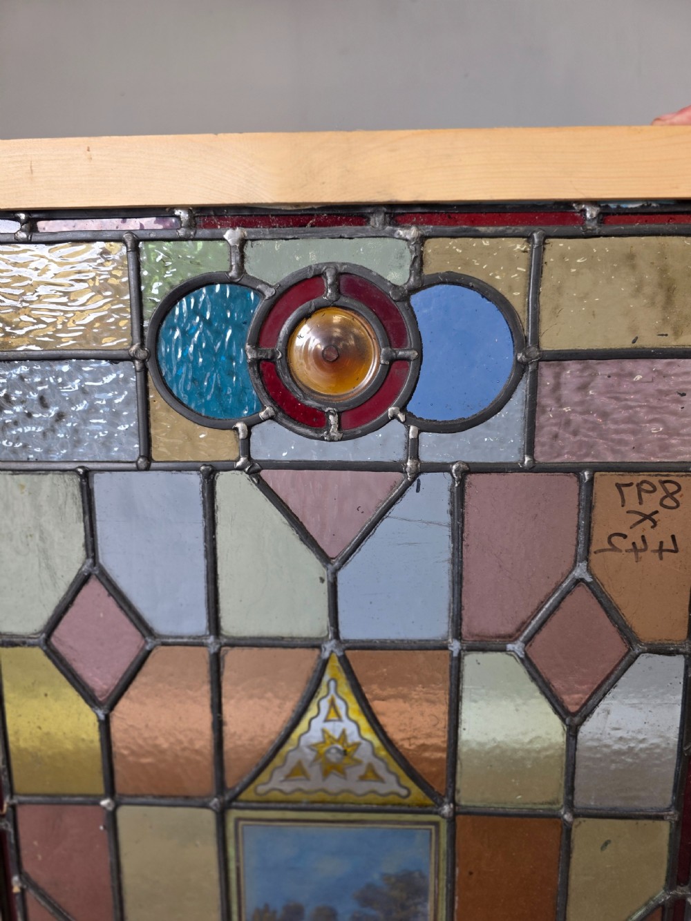 A rectangular leaded stained glass panel featuring geometric multicoloured glass sections and a central hand-painted country landscape. View III