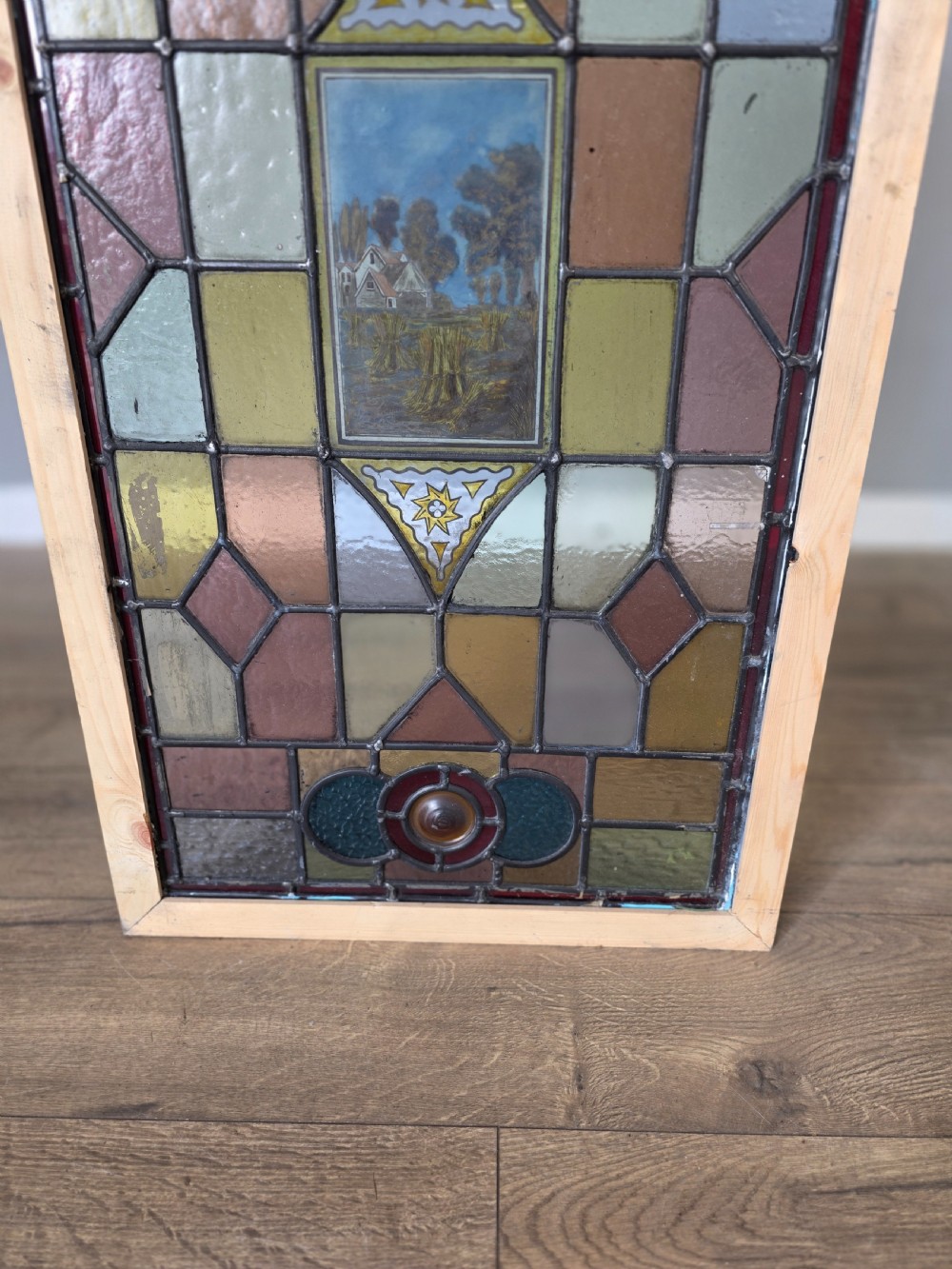 A rectangular leaded stained glass panel featuring geometric multicoloured glass sections and a central hand-painted country landscape. View IV
