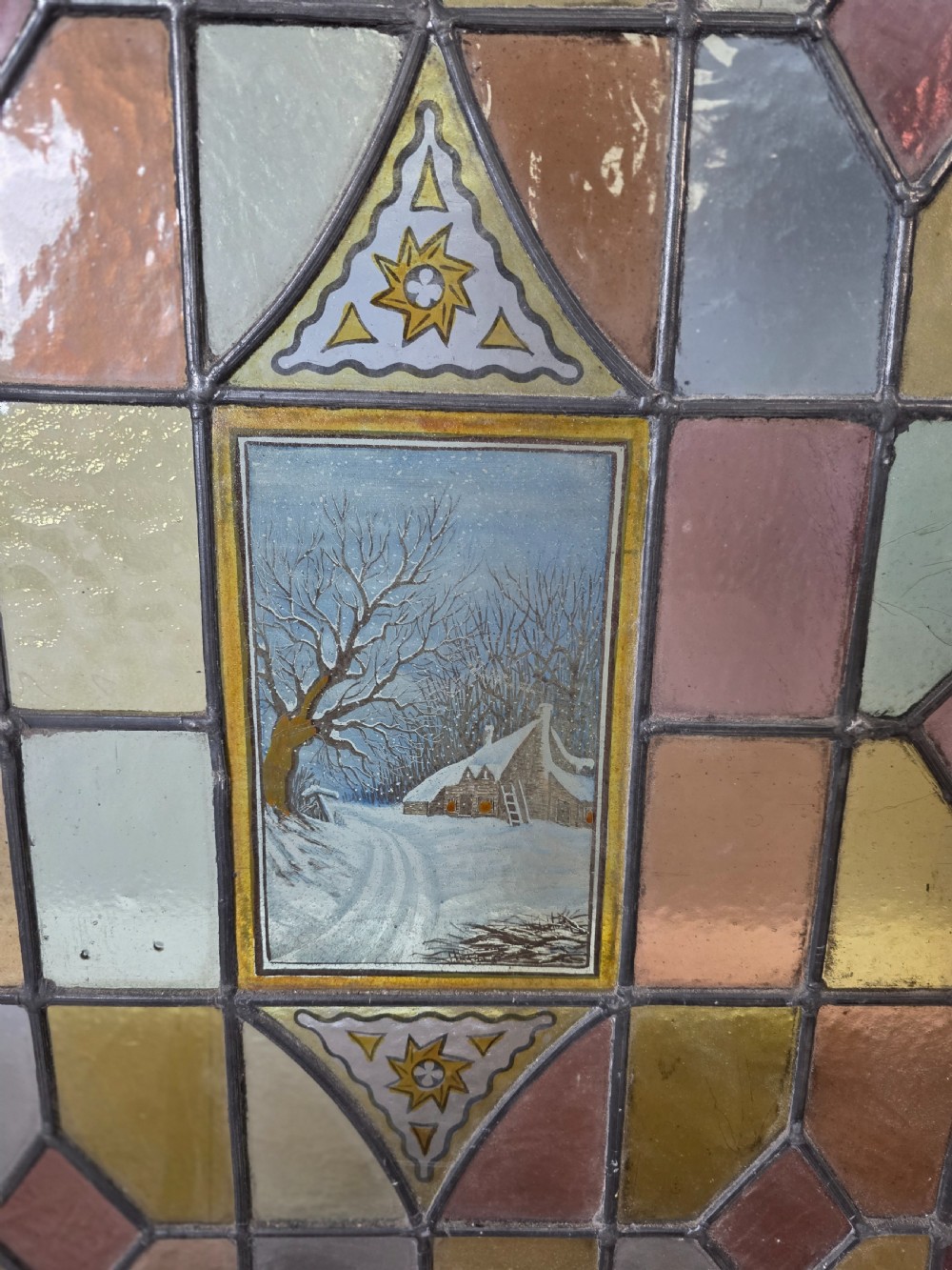 A rectangular Edwardian leaded stained glass window panel featuring geometric coloured glass, roundels, and a central hand-painted winter landscape scene set in a pine frame. View II