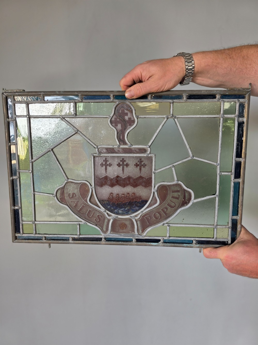 A rectangular Victorian leaded glass window panel featuring a central hand-painted heraldic coat of arms with the Latin motto Salus Populi.