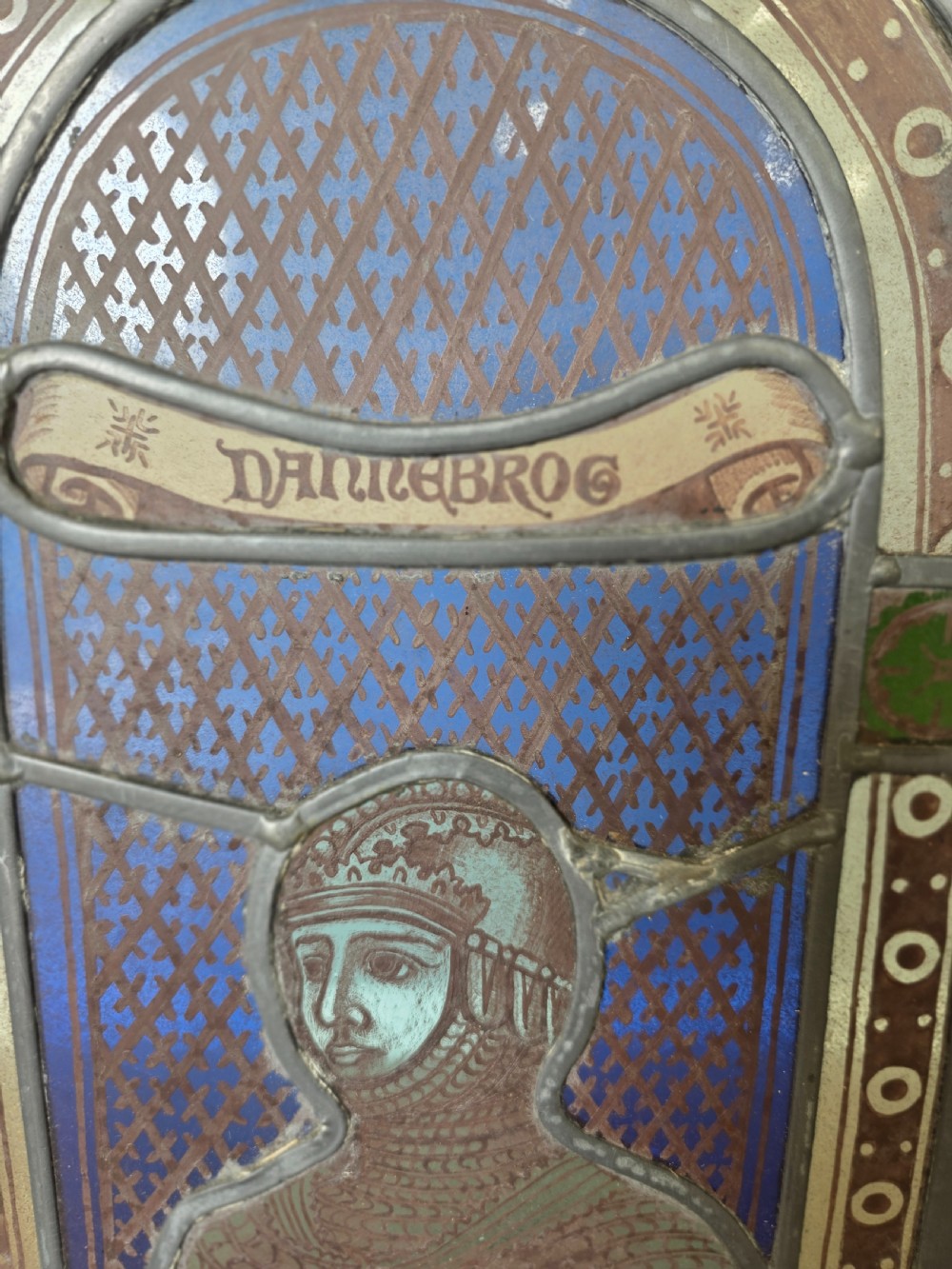 A rectangular leaded glass window panel featuring a central hand-painted figure of a knight in armour against a patterned blue background, encased in a simple pine frame. View V