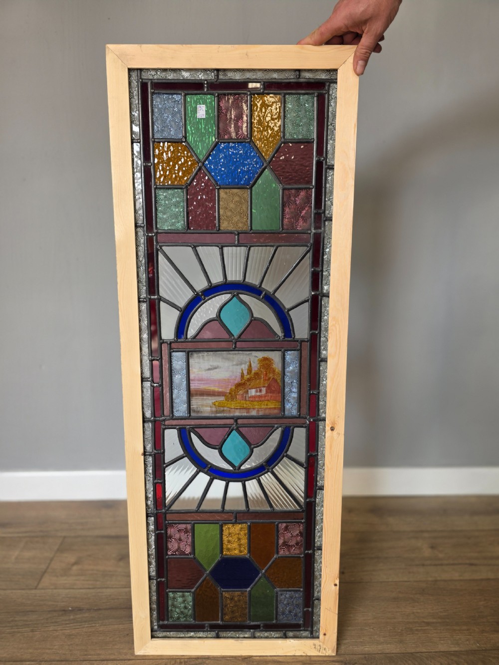 An elongated rectangular leaded glass panel featuring a central hand-painted landscape scene surrounded by geometric coloured glass borders. View II
