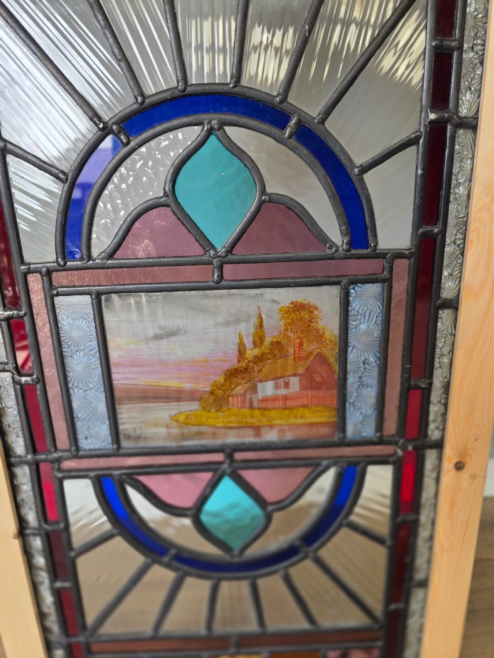 An elongated rectangular leaded glass panel featuring a central hand-painted landscape scene surrounded by geometric coloured glass borders. View III