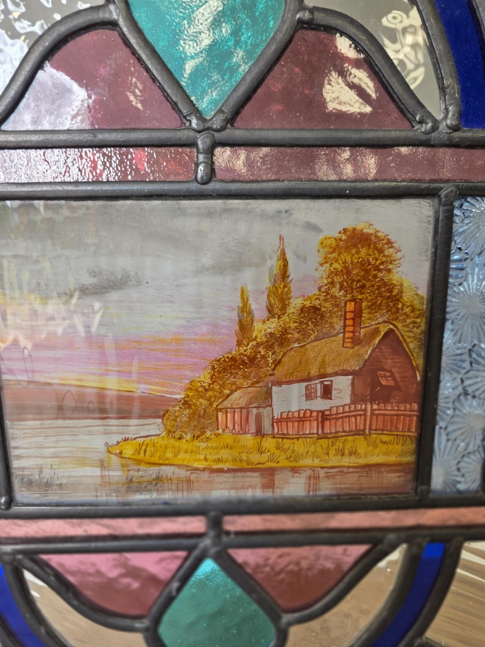 An elongated rectangular leaded glass panel featuring a central hand-painted landscape scene surrounded by geometric coloured glass borders. View VI