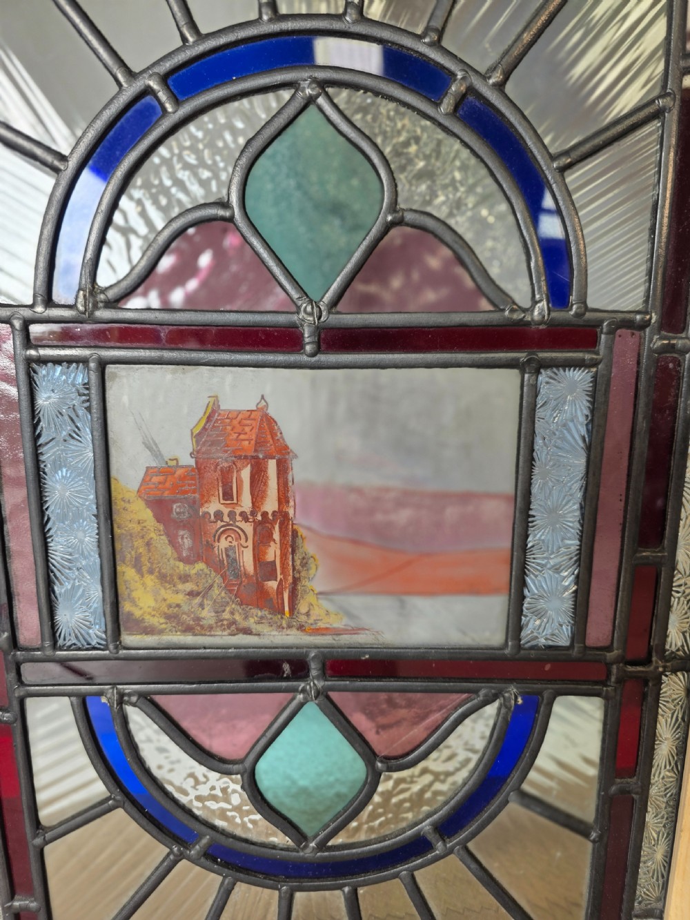 A vertical rectangular leaded glass panel featuring colourful geometric borders, textured glass panes, and a central hand-painted landscape scene. View II