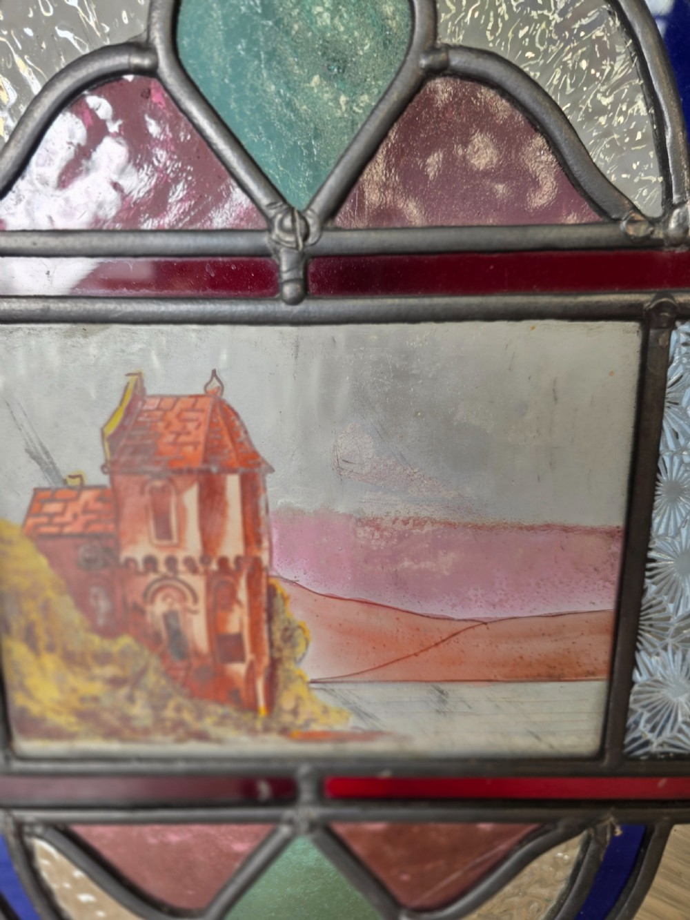 A vertical rectangular leaded glass panel featuring colourful geometric borders, textured glass panes, and a central hand-painted landscape scene. View III