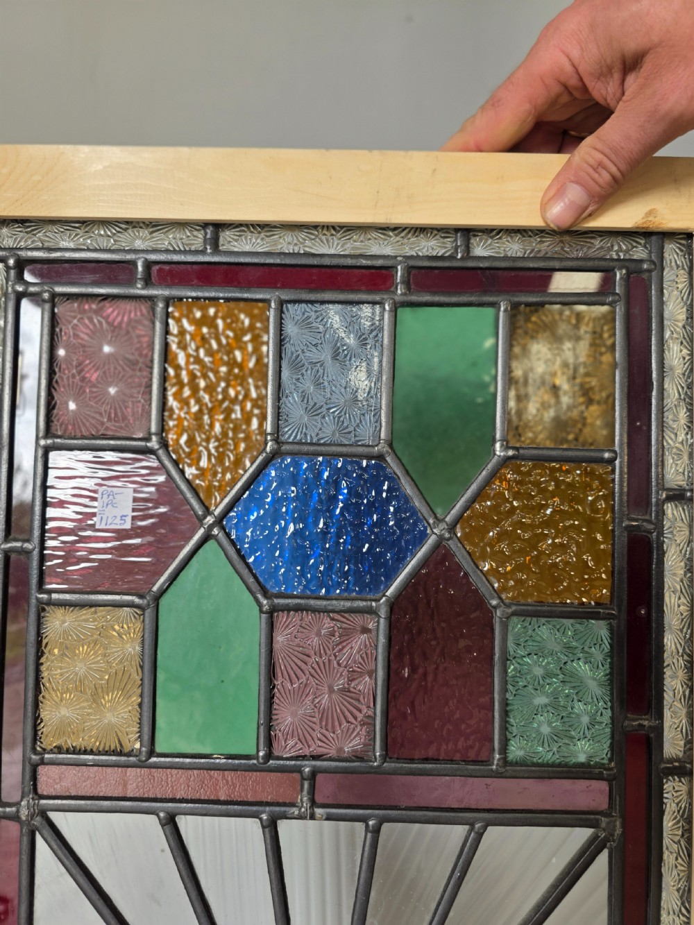 A vertical rectangular leaded glass panel featuring colourful geometric borders, textured glass panes, and a central hand-painted landscape scene. View IV