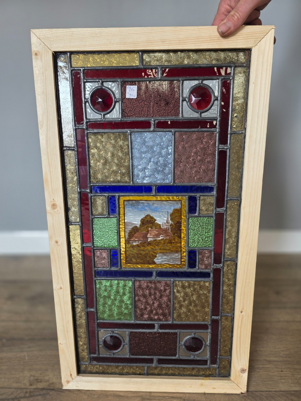 An antique rectangular leaded glass panel featuring colourful geometric textured borders around a central hand-painted countryside landscape scene depicting a church. View VII