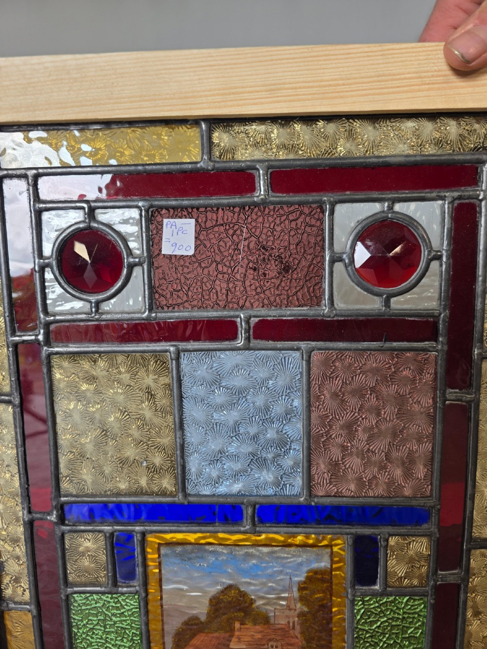 An antique rectangular leaded glass panel featuring colourful geometric textured borders around a central hand-painted countryside landscape scene depicting a church. View VIII