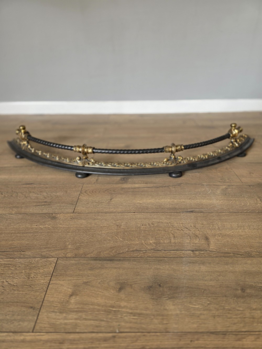 A 19th-century curved fire fender with a twisted black iron top rail and cast bronze foliate decoration.