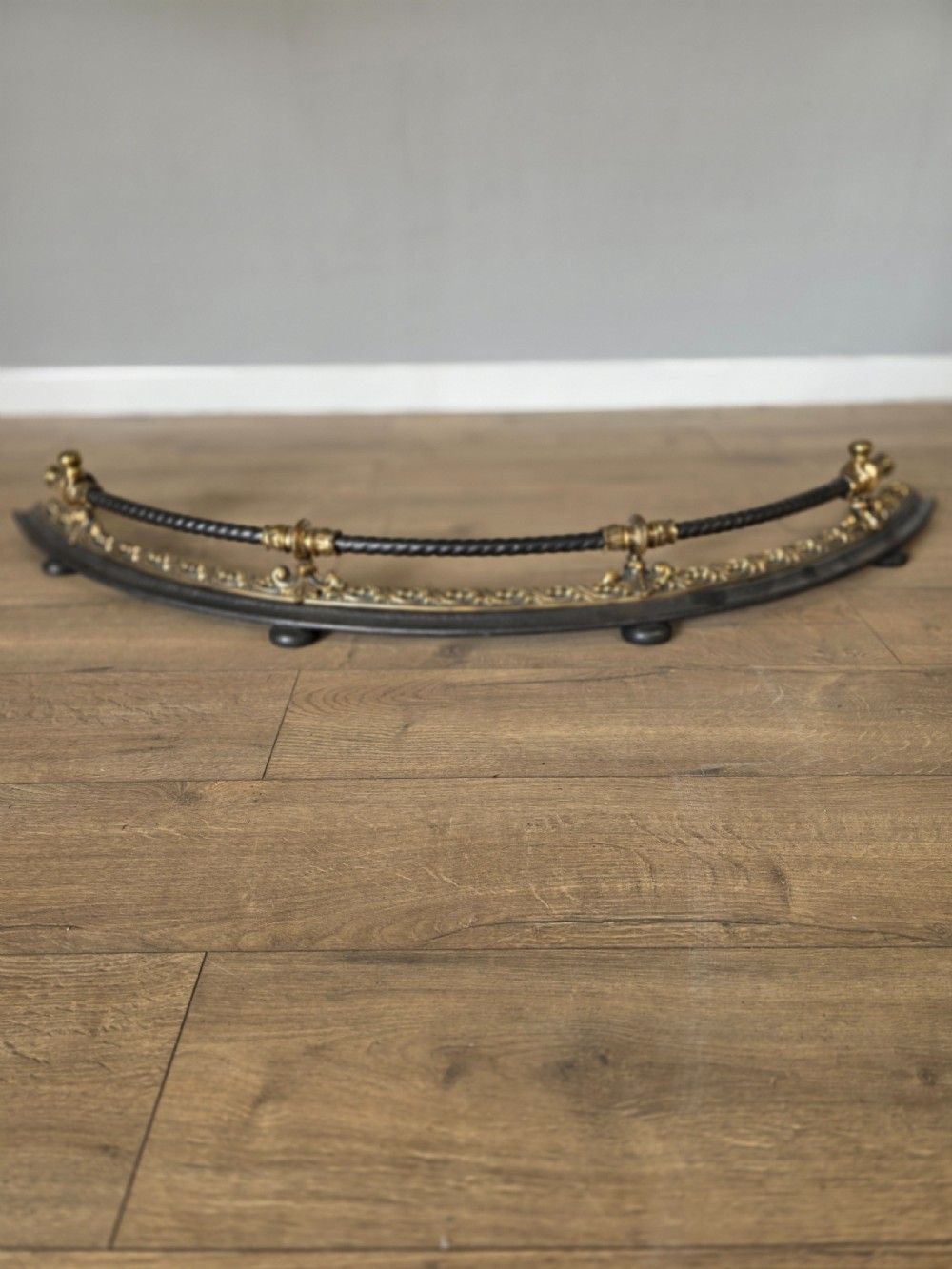 A 19th-century curved fire fender with a twisted black iron top rail and cast bronze foliate decoration. View II