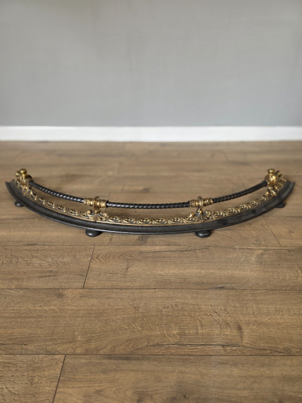 A 19th-century curved fire fender with a twisted black iron top rail and cast bronze foliate decoration. View III