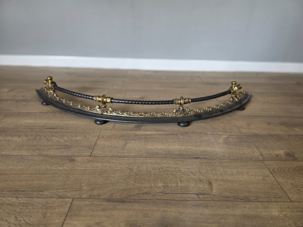 A 19th-century curved fire fender with a twisted black iron top rail and cast bronze foliate decoration. View V