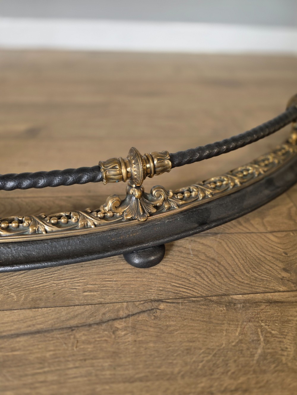 A 19th-century curved fire fender with a twisted black iron top rail and cast bronze foliate decoration. View VI