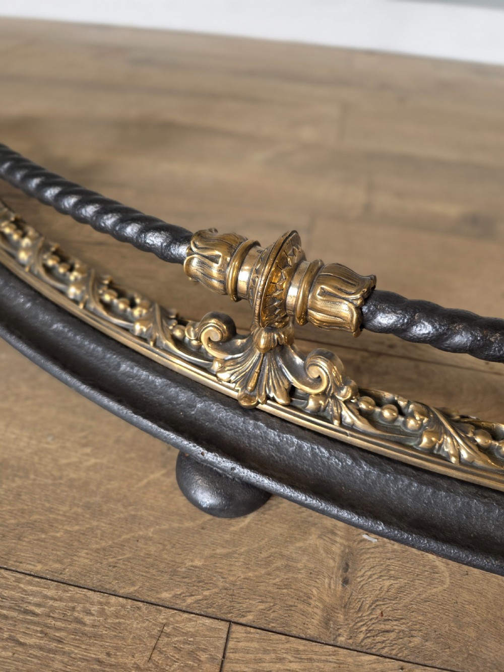 A 19th-century curved fire fender with a twisted black iron top rail and cast bronze foliate decoration. View VII