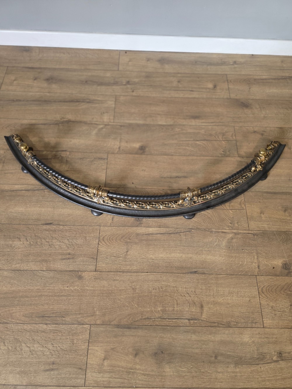A 19th-century curved fire fender with a twisted black iron top rail and cast bronze foliate decoration. View X