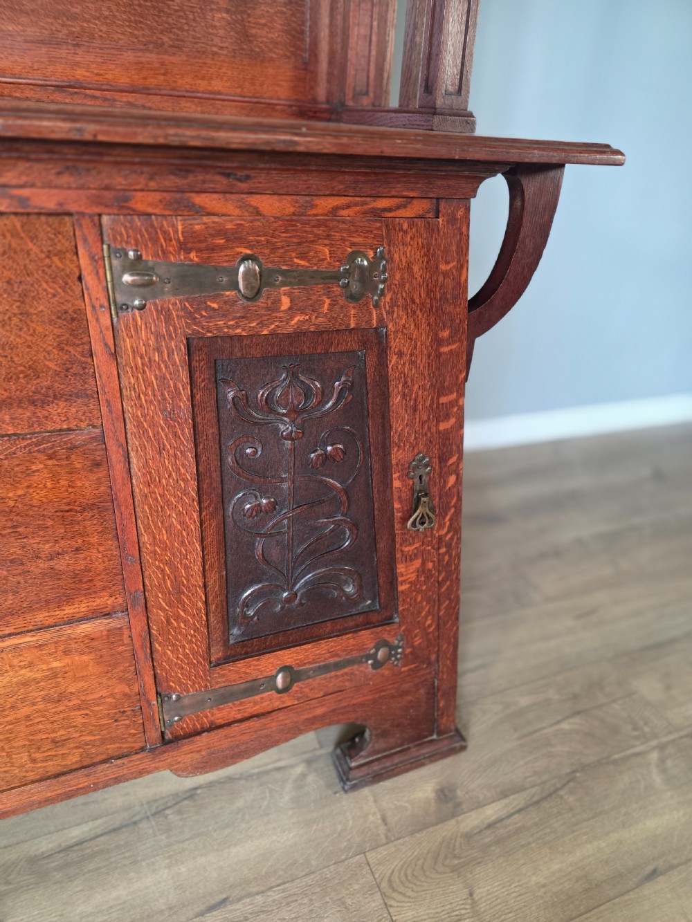 An Arts and Crafts quarter-sawn oak sideboard featuring hand-carved floral panels, copper strap hinges, central drawers, and a raised open shelf superstructure. View VII