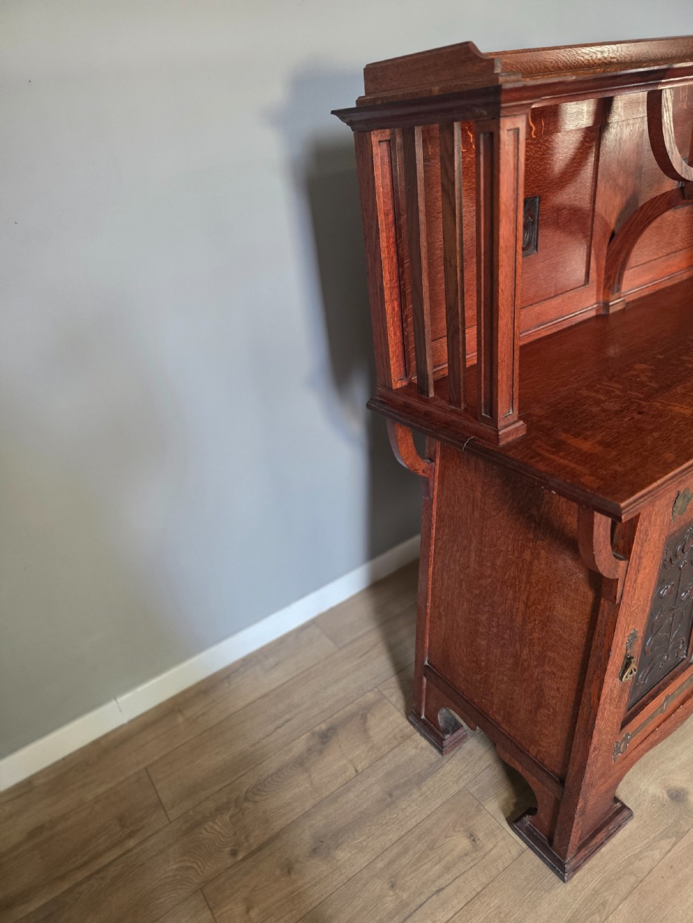 An Arts and Crafts quarter-sawn oak sideboard featuring hand-carved floral panels, copper strap hinges, central drawers, and a raised open shelf superstructure. View X