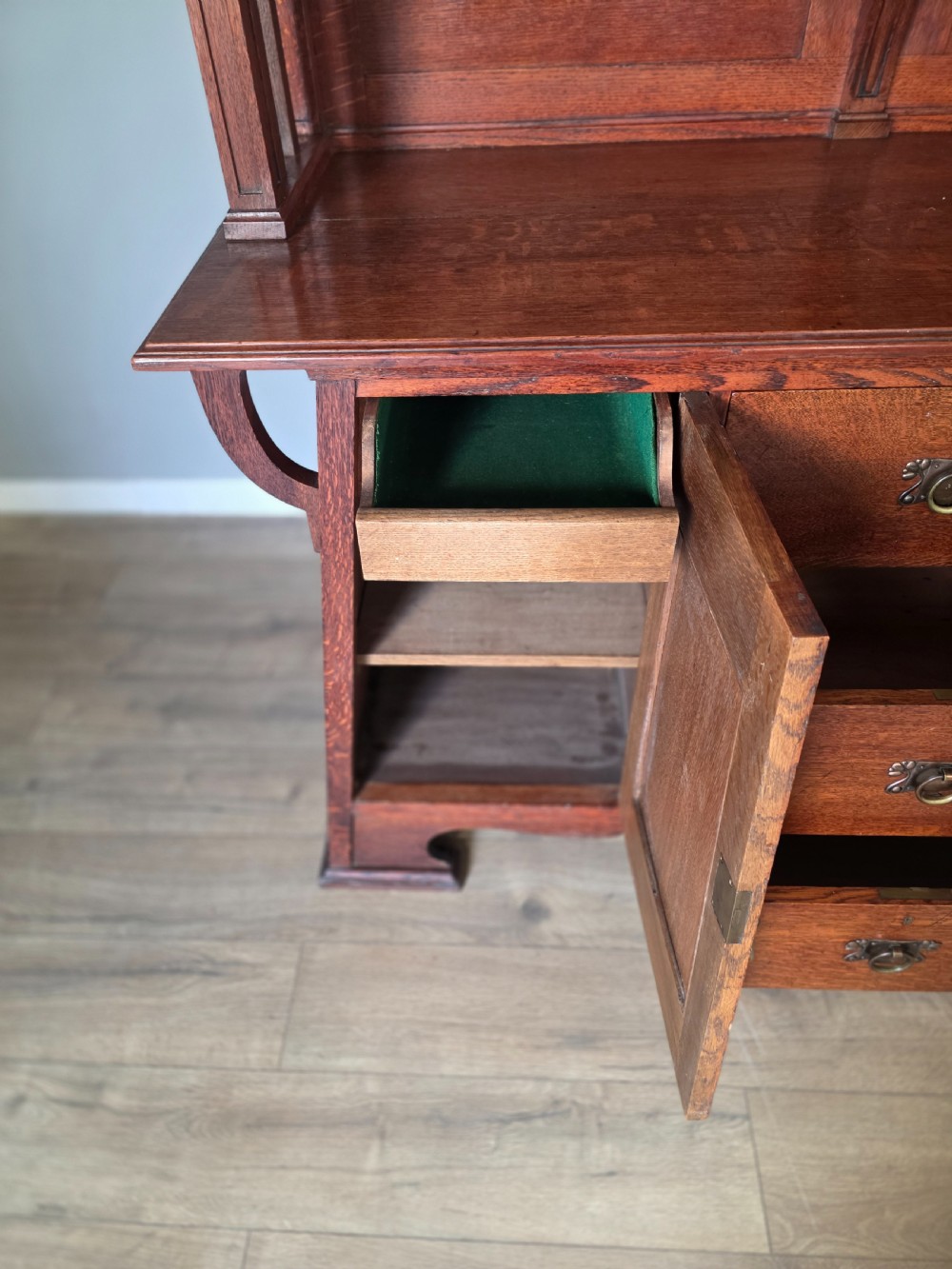 An Arts and Crafts quarter-sawn oak sideboard featuring hand-carved floral panels, copper strap hinges, central drawers, and a raised open shelf superstructure. View XVI