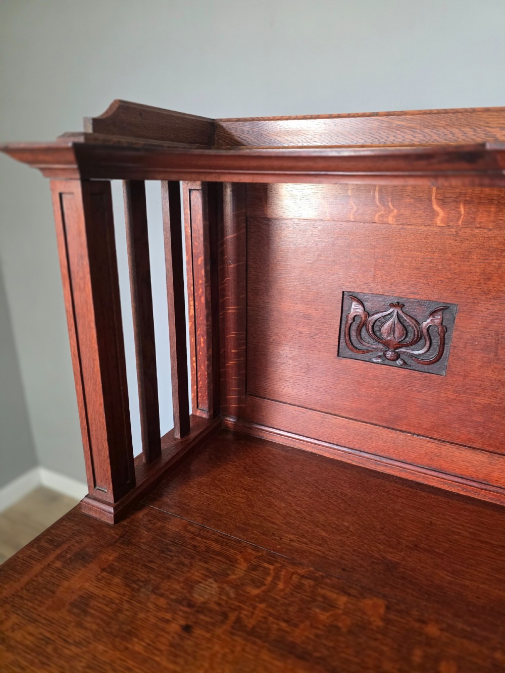 An Arts and Crafts quarter-sawn oak sideboard featuring hand-carved floral panels, copper strap hinges, central drawers, and a raised open shelf superstructure. View XVII