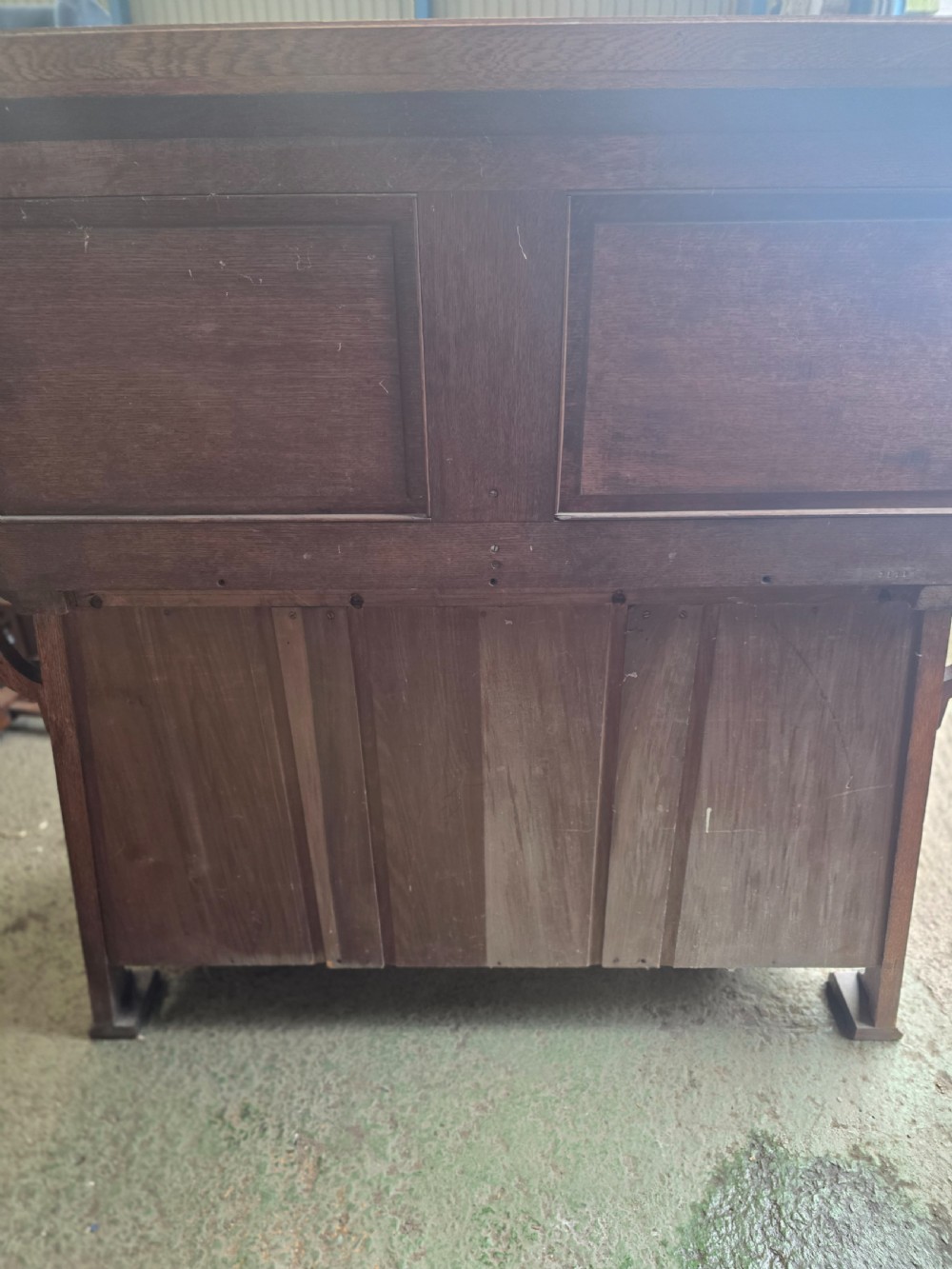 An Arts and Crafts quarter-sawn oak sideboard featuring hand-carved floral panels, copper strap hinges, central drawers, and a raised open shelf superstructure. View XXII