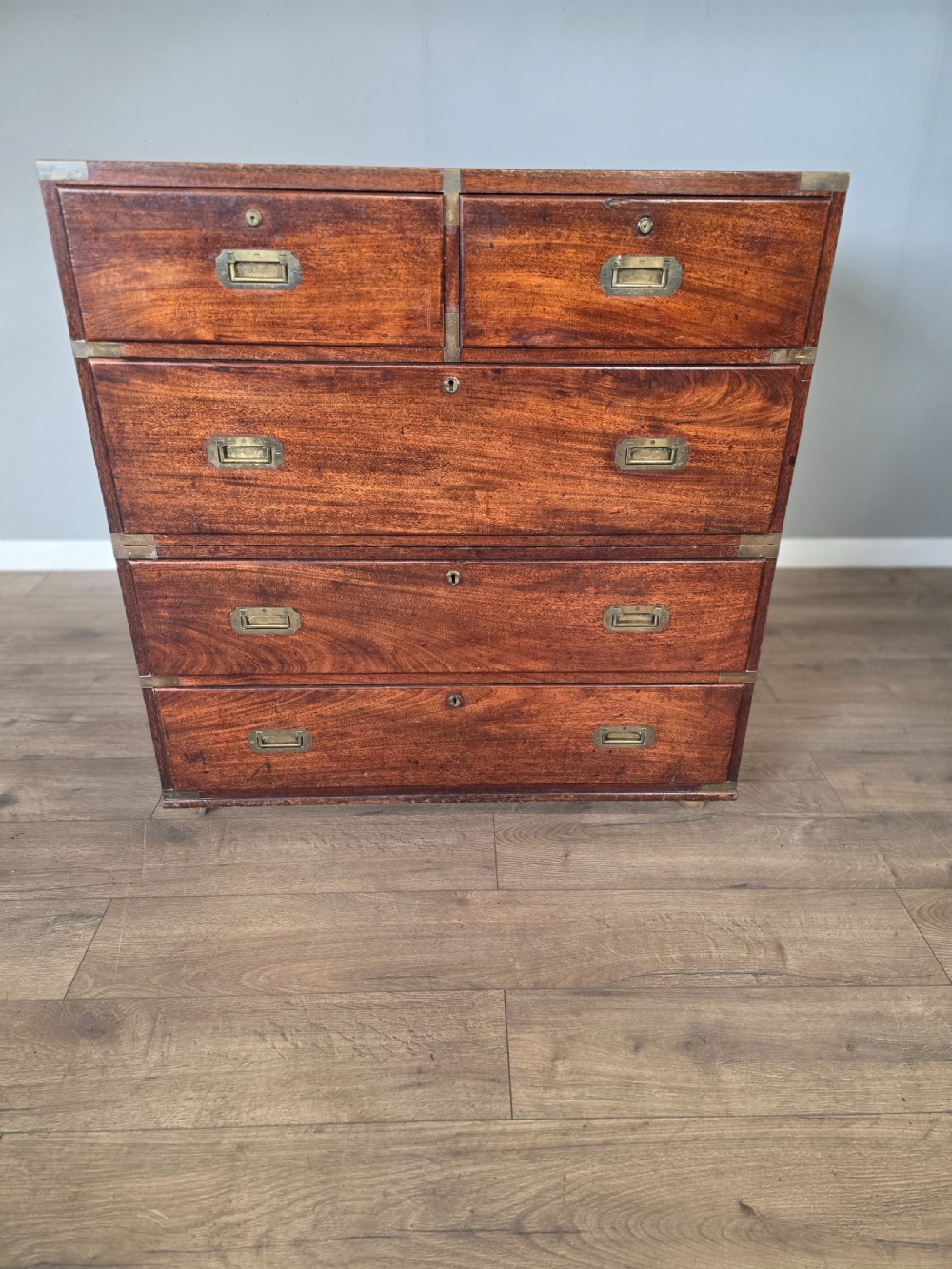 An 1830s Regency teak military campaign chest of drawers with flush brass corner brackets, strapwork, keyholes, and inset handles.