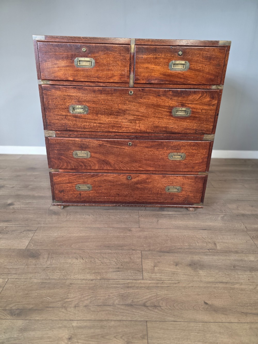 An 1830s Regency teak military campaign chest of drawers with flush brass corner brackets, strapwork, keyholes, and inset handles. View II