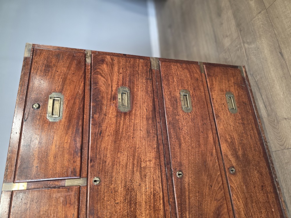 An 1830s Regency teak military campaign chest of drawers with flush brass corner brackets, strapwork, keyholes, and inset handles. View V