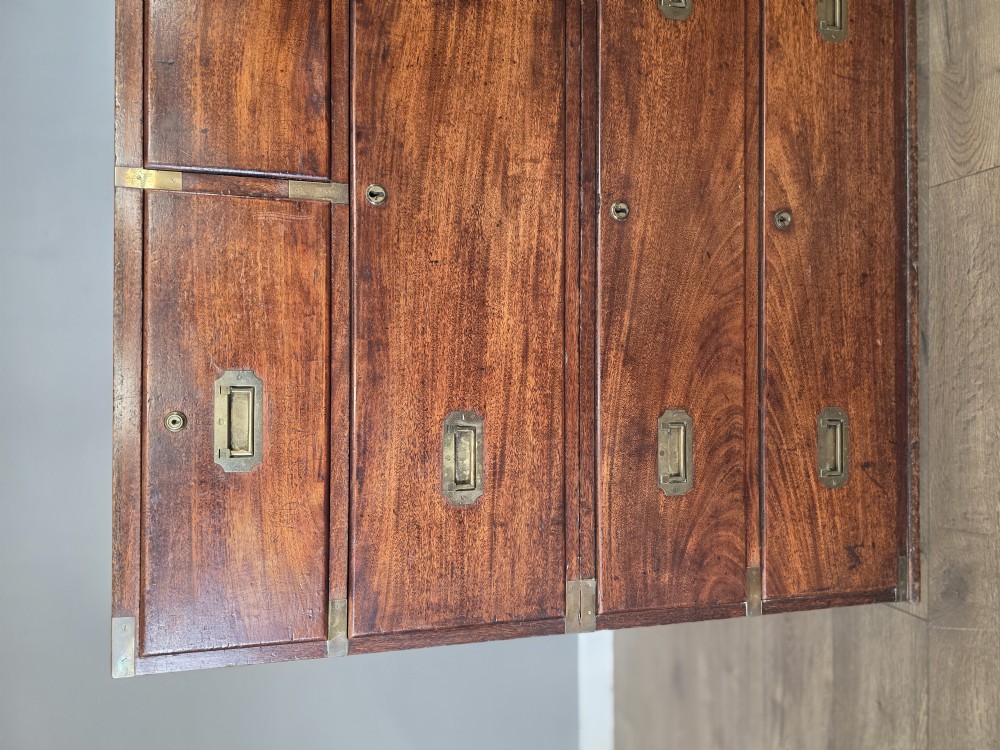 An 1830s Regency teak military campaign chest of drawers with flush brass corner brackets, strapwork, keyholes, and inset handles. View VI