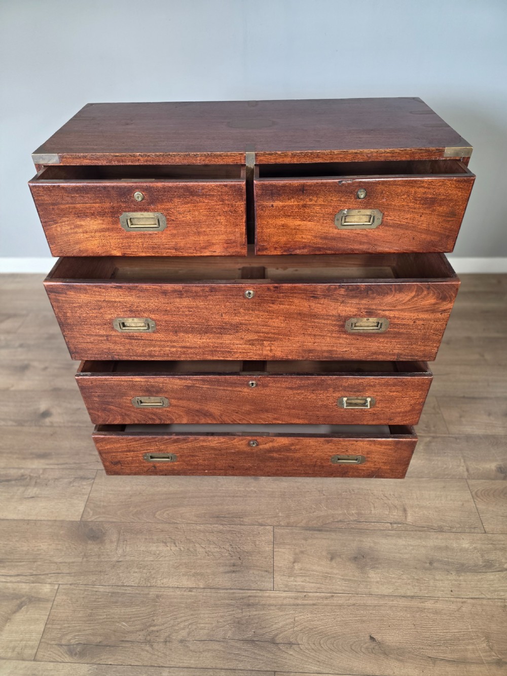 An 1830s Regency teak military campaign chest of drawers with flush brass corner brackets, strapwork, keyholes, and inset handles. View VII