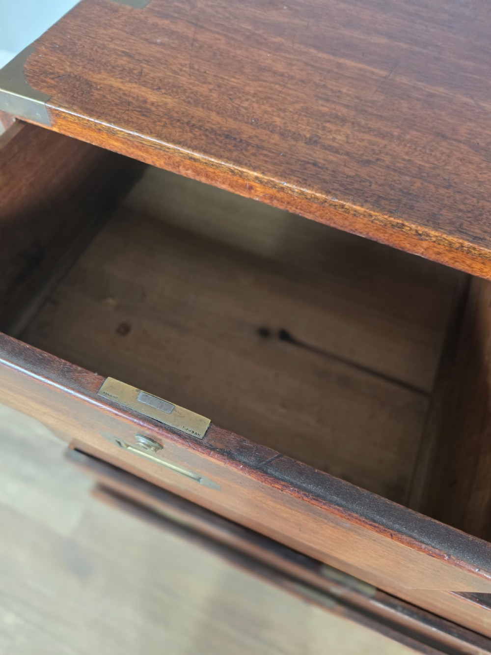 An 1830s Regency teak military campaign chest of drawers with flush brass corner brackets, strapwork, keyholes, and inset handles. View VIII