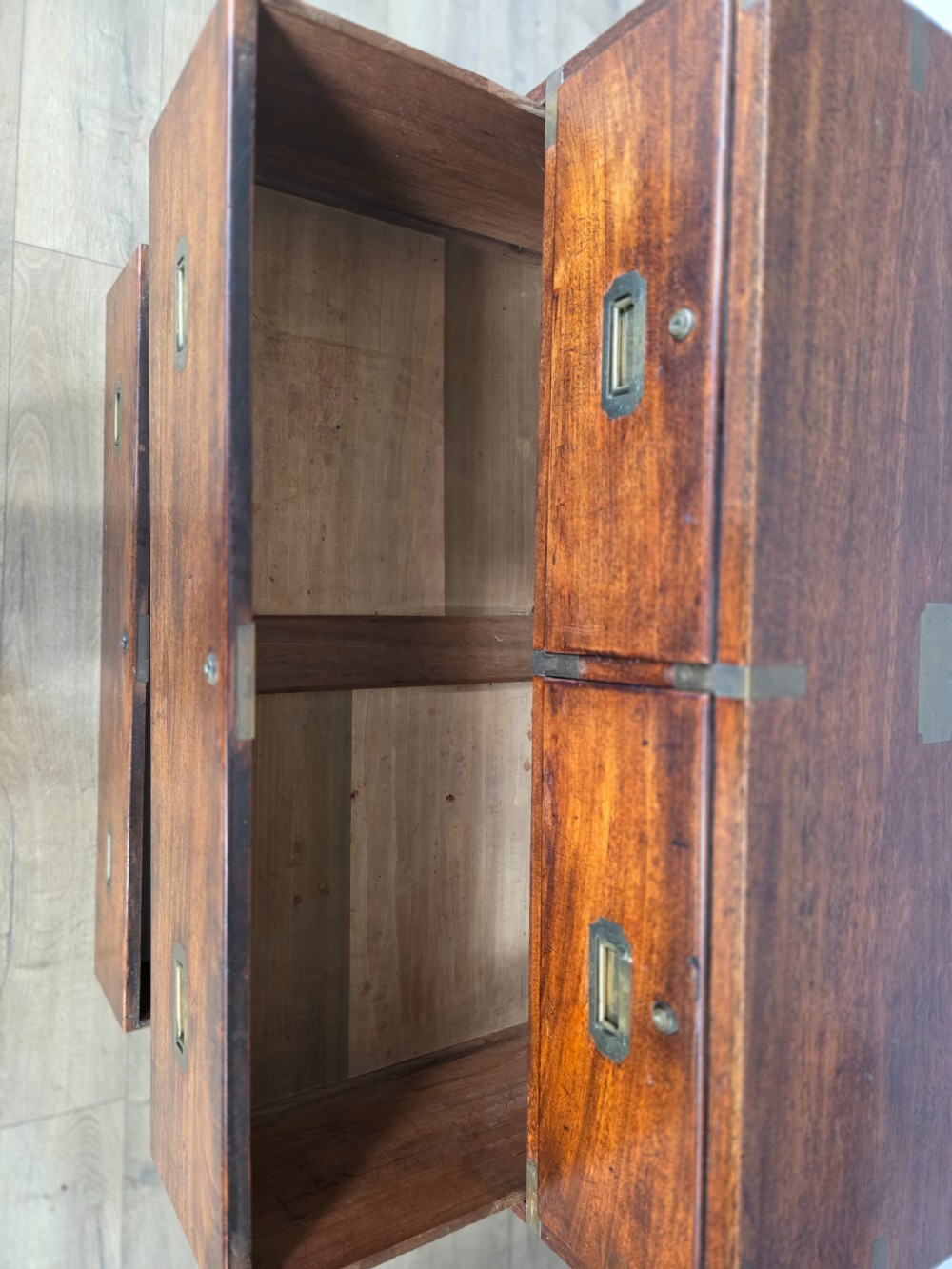 An 1830s Regency teak military campaign chest of drawers with flush brass corner brackets, strapwork, keyholes, and inset handles. View IX