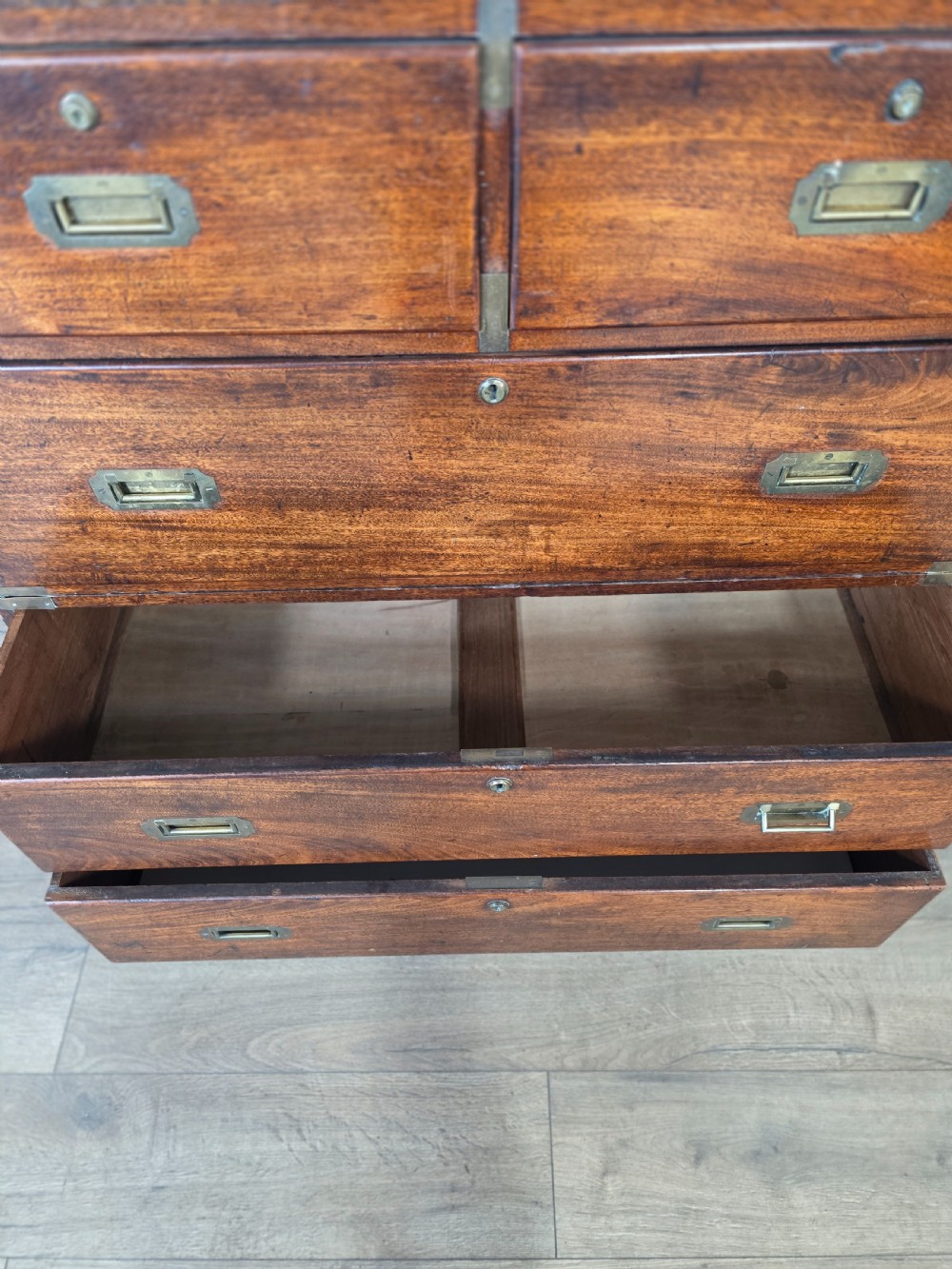 An 1830s Regency teak military campaign chest of drawers with flush brass corner brackets, strapwork, keyholes, and inset handles. View X