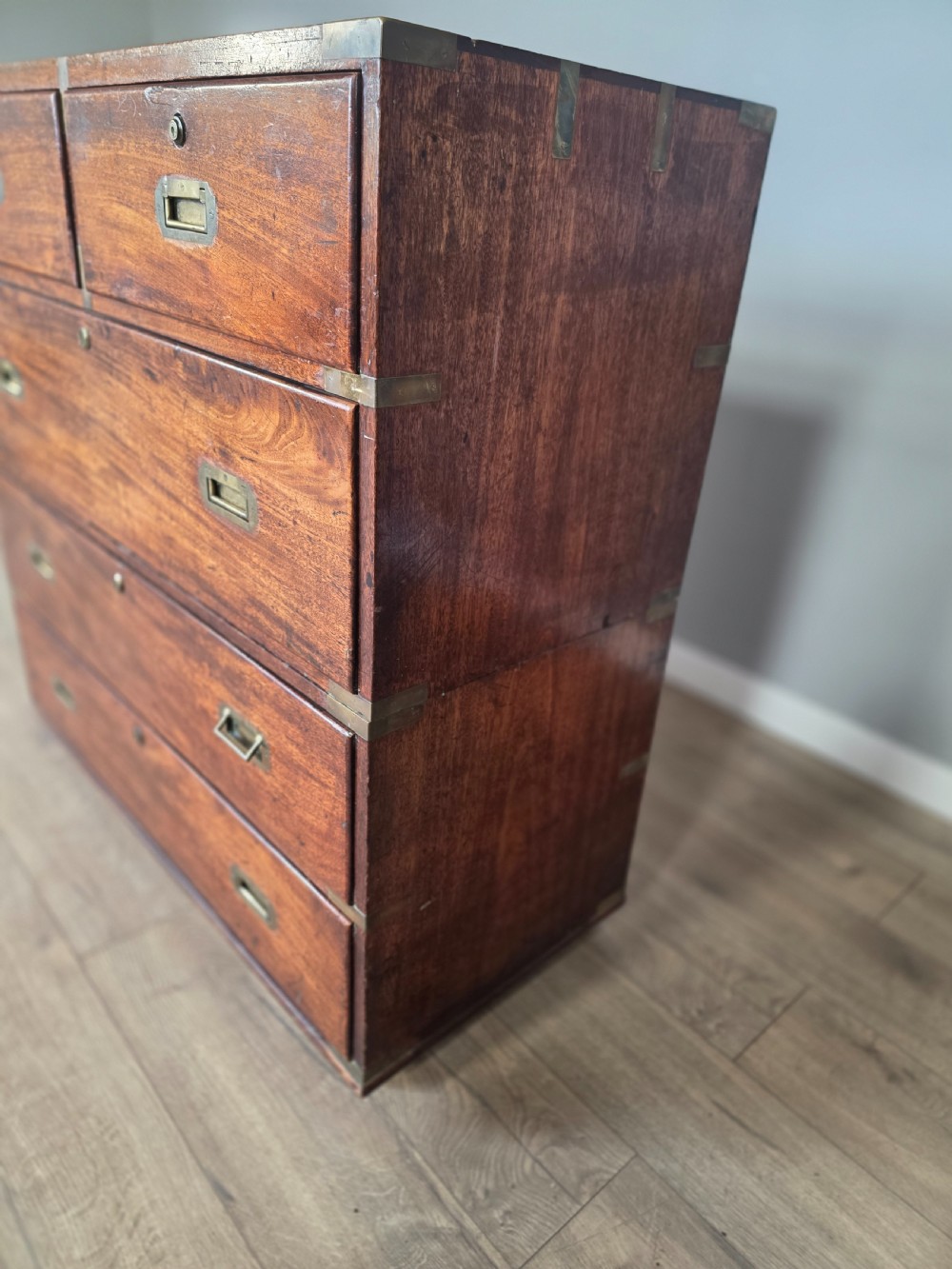 An 1830s Regency teak military campaign chest of drawers with flush brass corner brackets, strapwork, keyholes, and inset handles. View XII