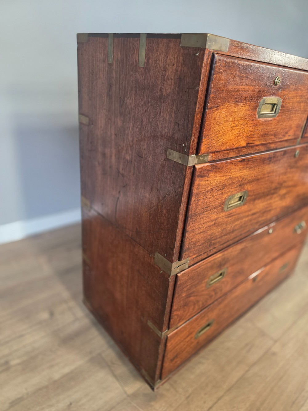 An 1830s Regency teak military campaign chest of drawers with flush brass corner brackets, strapwork, keyholes, and inset handles. View XIII